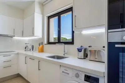 a white kitchen with a sink and a window at Pine Cliffs Village in Albufeira