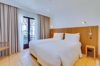 a bedroom with a large white bed and a window at Pine Cliffs Village in Albufeira