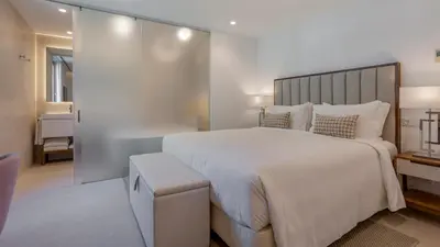 a white bedroom with a large bed and a bathroom at Pine Cliffs Village in Albufeira