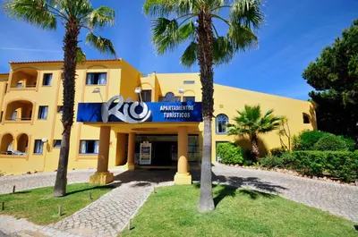a yellow building with palm trees in front of it at Rio by Garvetur in Vilamoura