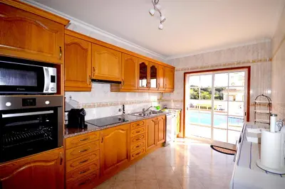 a kitchen with wooden cabinets and a large window at magnifique et spacieuse villa avec piscine privative in Albufeira
