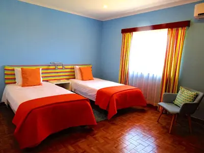 a room with two beds and a chair and a window at Villa Esmeralda in Albufeira