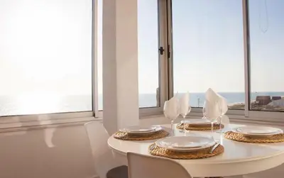 a white dining table with white chairs and windows at Ria Beach House in Faro