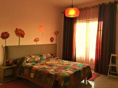 a bedroom with a bed and a window with flowers on the wall at Excelente T1 Oura Beach Bicos Apartment Lucia in Albufeira