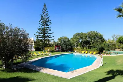 a large swimming pool in a park with a tree at Casa Moura Golfe in Vilamoura