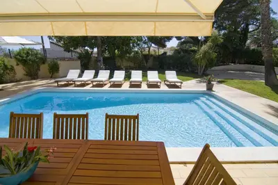 a swimming pool with chairs and a table and an umbrella at Villa Jasmim in Almancil