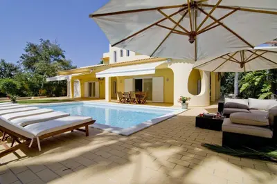 a house with a swimming pool with an umbrella at Villa Jasmim in Almancil
