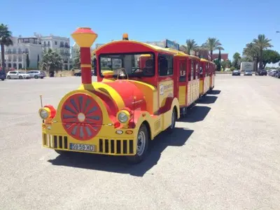 a small red and yellow train parked in a parking lot at Quarteira Beach in Quarteira
