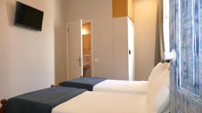 a bedroom with two beds and a tv on a wall at Guest House Sao Filipe in Faro