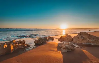 a sunset on a beach with rocks in the sand at Welcoming apartment in Albufeira 80 m² with shared pool in Albufeira