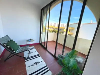 a room with a balcony with a chair and a plant at Apartamento bem localizado in Albufeira