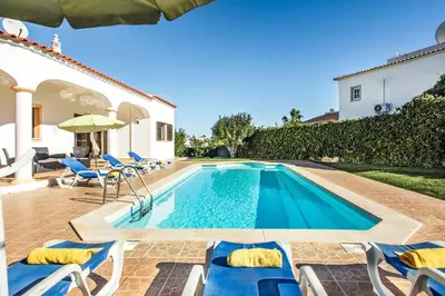 a swimming pool with chairs and a villa at Villa Lourenco in Albufeira