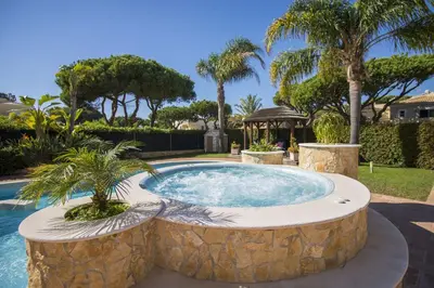 a swimming pool with a stone wall and palm trees at Villa Hera in Vilamoura