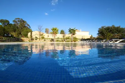 a swimming pool with blue water and palm trees at Pinheiros da Balaia Villas in Albufeira