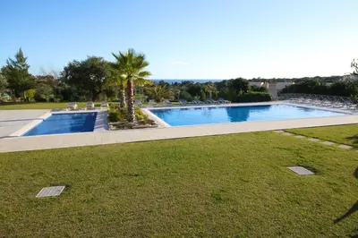 a swimming pool in a park with a grass field at Pinheiros da Balaia Villas in Albufeira