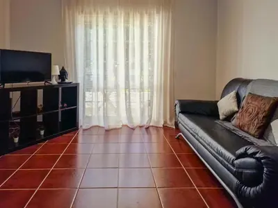 a living room with a black leather couch and a television at Falésia Beach Just 800 m (Apartment Surfal) in Roja- Pé