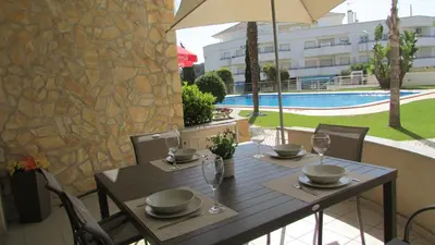 a wooden table with chairs and an umbrella and a pool at Pomba Branca (4-6 per.) Piscina, 500m Praia in Albufeira