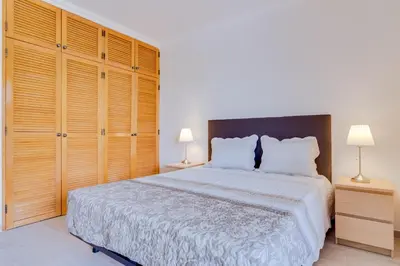 a bedroom with a large bed and wooden cabinets at Tália II - City Center - Vilamoura in Vilamoura