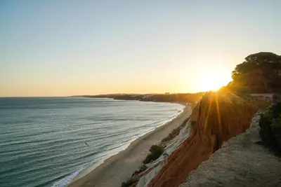 a beach with the sun setting over the ocean at Epic Falésia Apartment by The Portuguese Butler in Olhos de Água