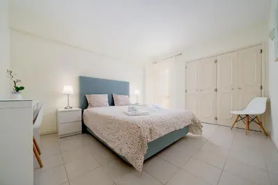 a white bedroom with a bed and a chair at AL - R&R Vilamoura Flat, City Center in Vilamoura