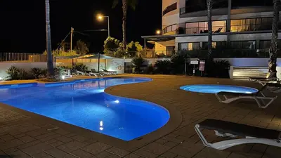 a swimming pool at night with chairs and a building at Cavalo Preto Luxury Beach Resort in Quarteira