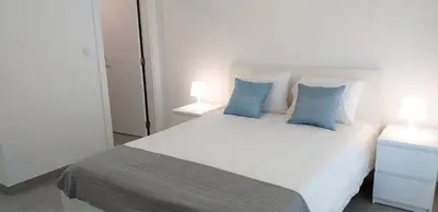 a white bed with two blue pillows in a bedroom at Lote 1 Aconchegante in Quarteira