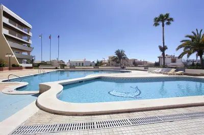 a swimming pool in a resort with palm trees and a building at O Apartamento A Ramos Palmeira Galé Está inserido num Condomínio com PISCINA, Fica apenas a 250 Metros da Praia da Galé - Apartamento com Ar Condicionado na Sala, Smart TV com Prime Vídeo e Cozinha Completa in Albufeira