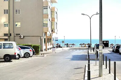 a street with cars parked next to a building and the ocean at Quarteira Beach Holidays in Quarteira