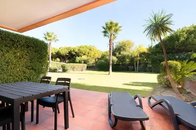 a patio with a table and chairs and palm trees at AL - Apartamentos Vila Sol F5 Bloco 3 in Quarteira