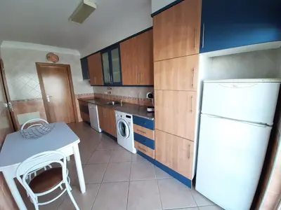 a small kitchen with a white refrigerator and a table at Apartamento Alfarrobeira Mar in Quarteira