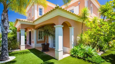 a pink house with palm trees in front of it at Villa Natura - Varandas do Lago in Almancil