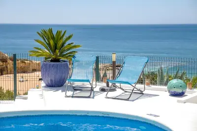 two chairs and a potted plant next to a swimming pool at Villa Front de Mer avec Piscine Jacuzzi Accès Privé Plage en famille et entre amis in Albufeira