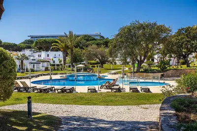 a swimming pool in a park with chairs and trees at Apartament Portes Balaia Golf Resort in Albufeira