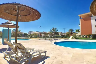 two chairs and an umbrella next to a swimming pool at Albufeira parque da CORCOVADA standing flat W/Pool in Albufeira