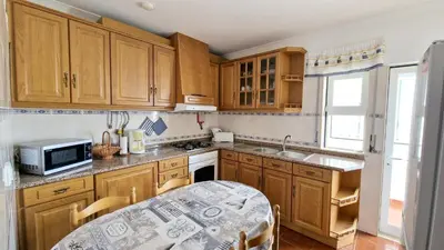a kitchen with wooden cabinets and a table and a microwave at Apartamento Carvalhal in Quarteira