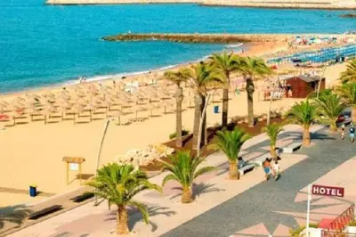 a beach with chairs and palm trees and the ocean at Apartamento Brás in Quarteira