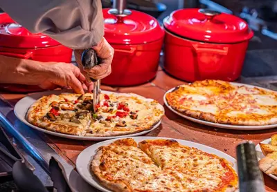 a person cutting a pizza with a pizza cutter at 3HB Guarana - All Inclusive in Albufeira