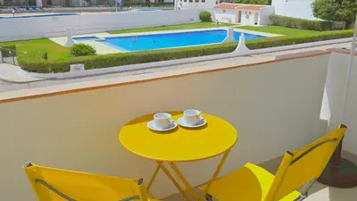 a yellow table with two cups and chairs and a pool at Praia Eulália with pool and 5 minutes from the beach in Albufeira