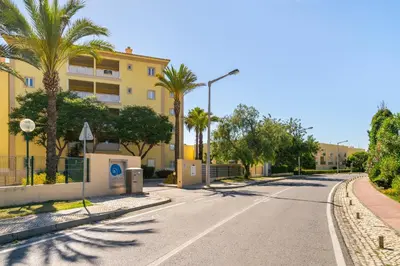a street with palm trees and a yellow building at WHome | Vilamoura Family Apartment in Quarteira