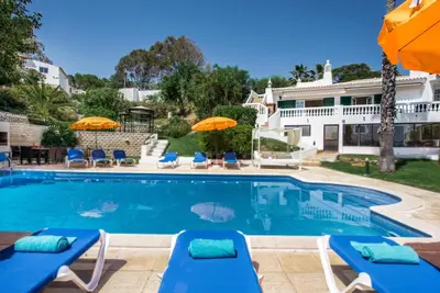 a swimming pool with chairs and umbrellas next to a house at Forte São João Villas da Praia in Albufeira