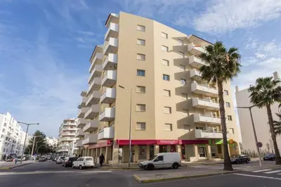 a tall building on a city street with cars parked at Apartamento Millenium Vista Mar- 2 passos da Praia in Quarteira