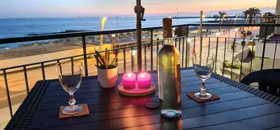 a table with candles and glasses on a balcony with the beach at Lusitania T2 Frente Mar em Quarteira in Quarteira