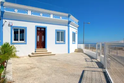 a white house with a red door next to the ocean at Casa da Bandeira -Perfect Location-Beach front- Rooftop Pool by DreamvillasAlbufeira in Albufeira
