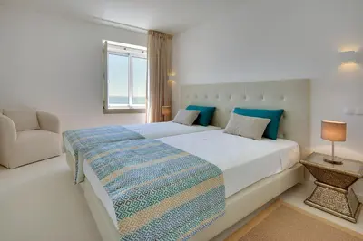 a white bedroom with a large bed and a chair at Casa da Bandeira -Perfect Location-Beach front- Rooftop Pool by DreamvillasAlbufeira in Albufeira