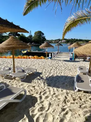 a sandy beach with chairs and umbrellas and the water at Beautiful apartment for rent in Quinta do Lago with excellent resort facilities close to lake and beach. in Quinta do Lago