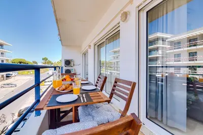 a balcony with a wooden table and chairs and a window at Colina Sol T2 Quarteira Beach in Quarteira