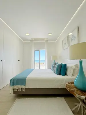 a white bedroom with a large bed and a window at Seafront Apartment in Quarteira in Quarteira