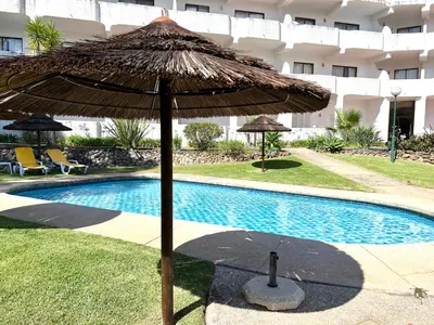 a large straw umbrella next to a swimming pool at Sea Gardens - Alvaflor - Vilamoura in Vilamoura