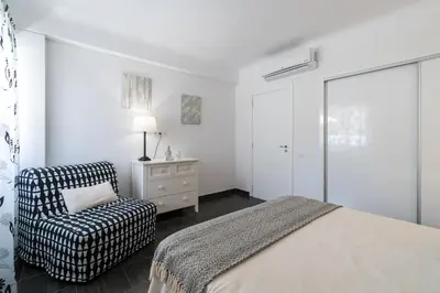 a white bedroom with a bed and a chair at Serenity by Intiholidays in Quarteira