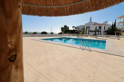a swimming pool with a straw umbrella and a resort at Olhos De Água 1BR with Pool, AC and Free Parking in Albufeira